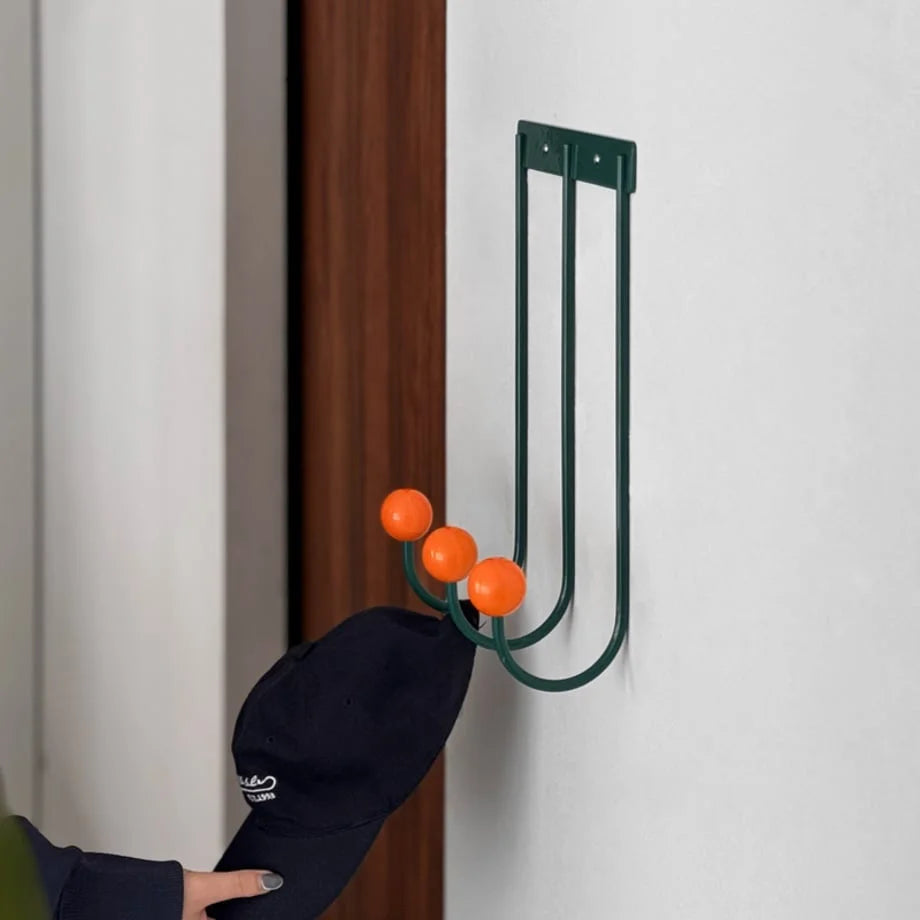 Close-up detail of the Green & Orange metal coat rack with a dark cap hanging from it. - RoomDen