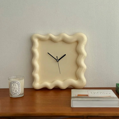 Direct front view of the cream Wavy Squiggle Frame Clock on a wooden surface. - RoomDen