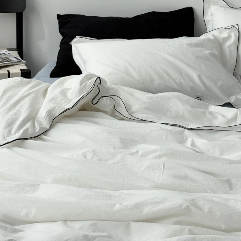 Close-up of pillows on a white ruffled bedding set with black piped edges. - RoomDen