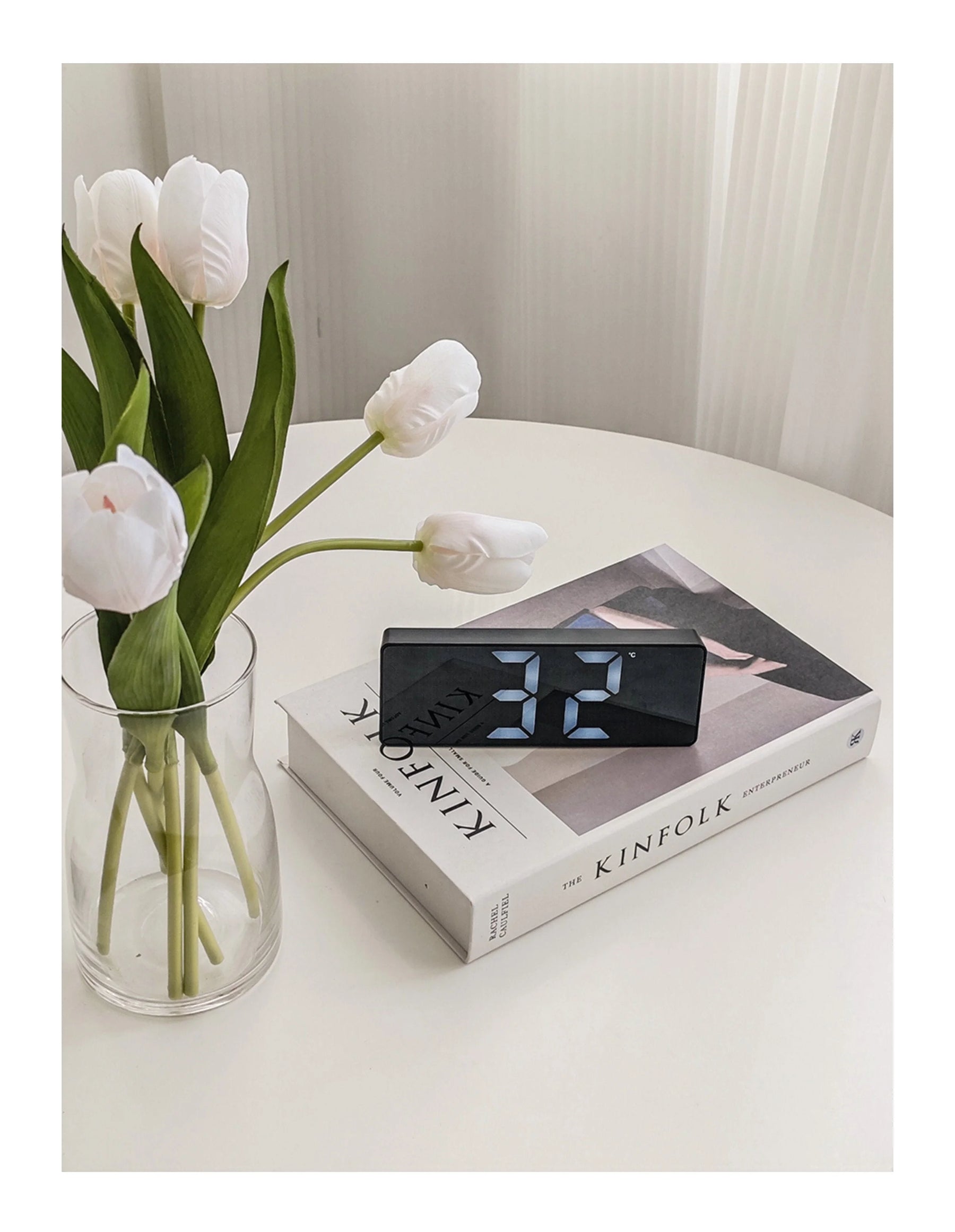 The black Sleek Mirrored LED Table Clock styled on a Kinfolk book next to white tulips in a vase. - RoomDen