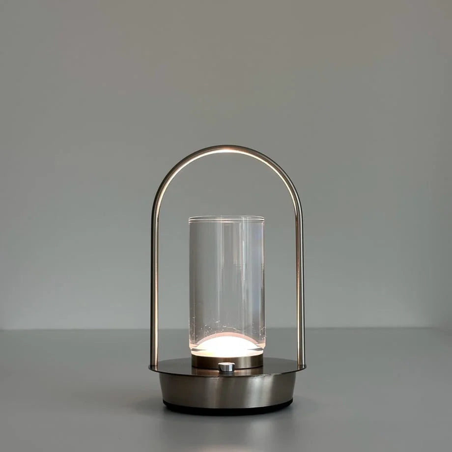 The Minimalist Arch Metal Portable Table Lamp turned on with a natural, soft white light. - RoomDen