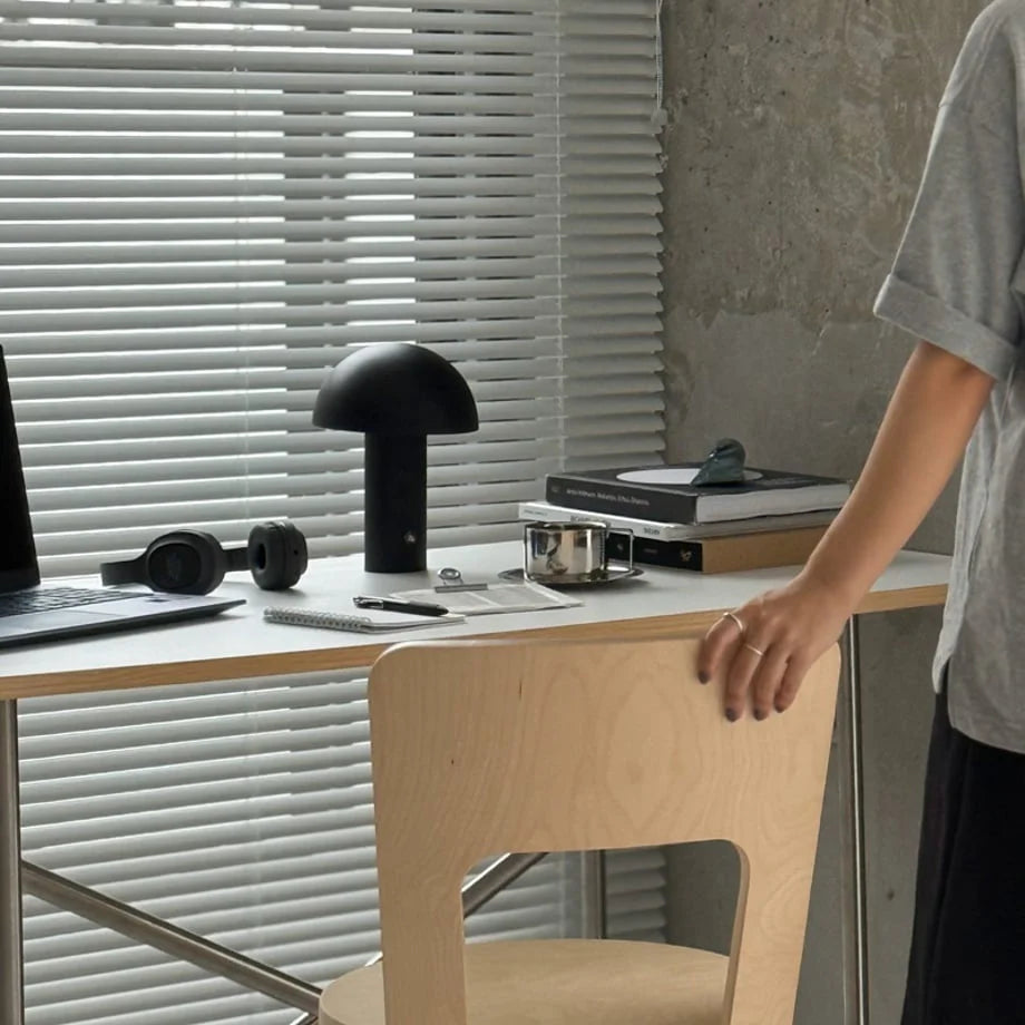 A wide view of a modern workspace featuring the black mushroom table lamp on a light wood desk - RoomDen.