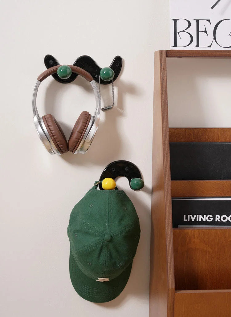 Headphones and a green baseball cap hanging from black wavy and U-shaped ceramic hooks on a wall.
