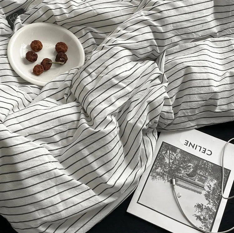 Close-up of the soft, rumpled texture of the white and black pinstripe washed cotton duvet cover with a magazine and snack. - RoomDen
