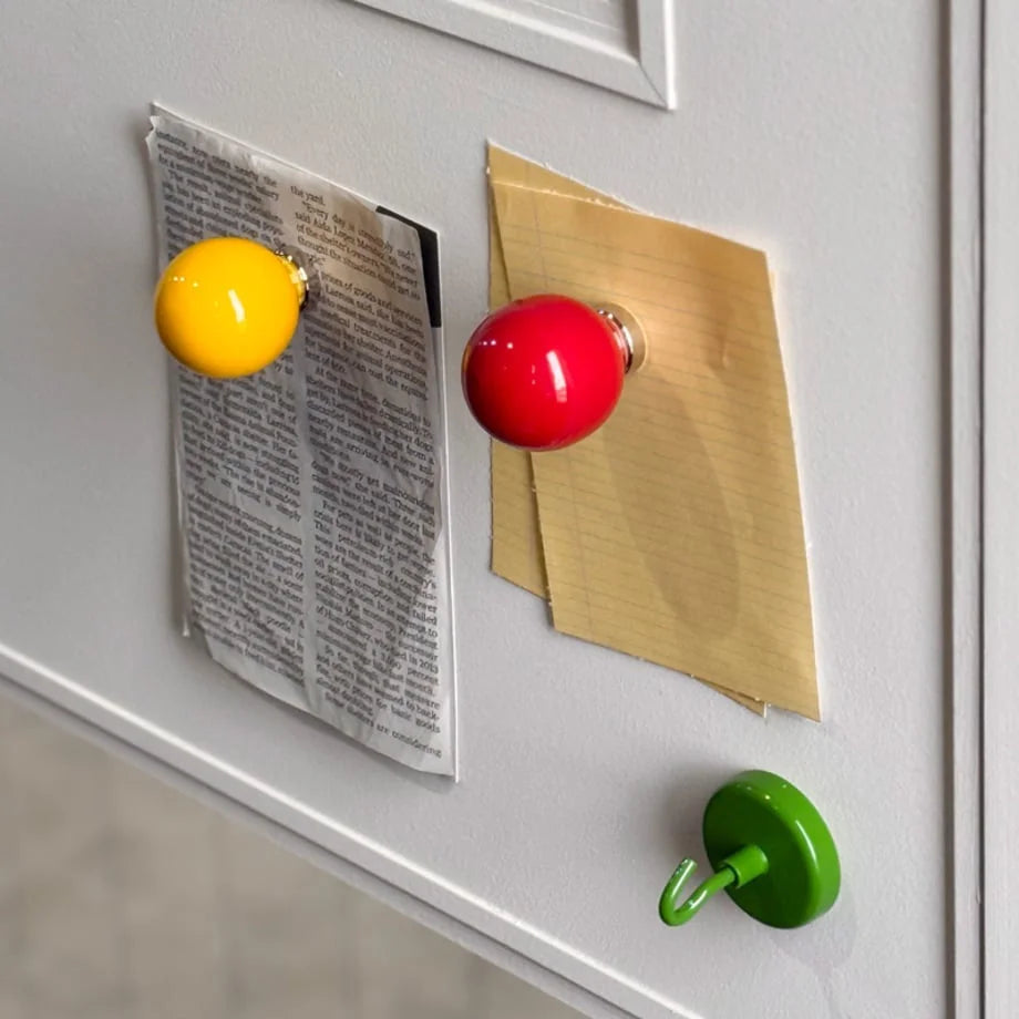 Yellow and red magnetic ball hooks holding papers on a grey metal door. - RoomDen