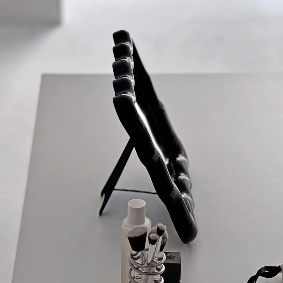 Side view of the black wavy mirror showing the slim profile and easel stand - RoomDen