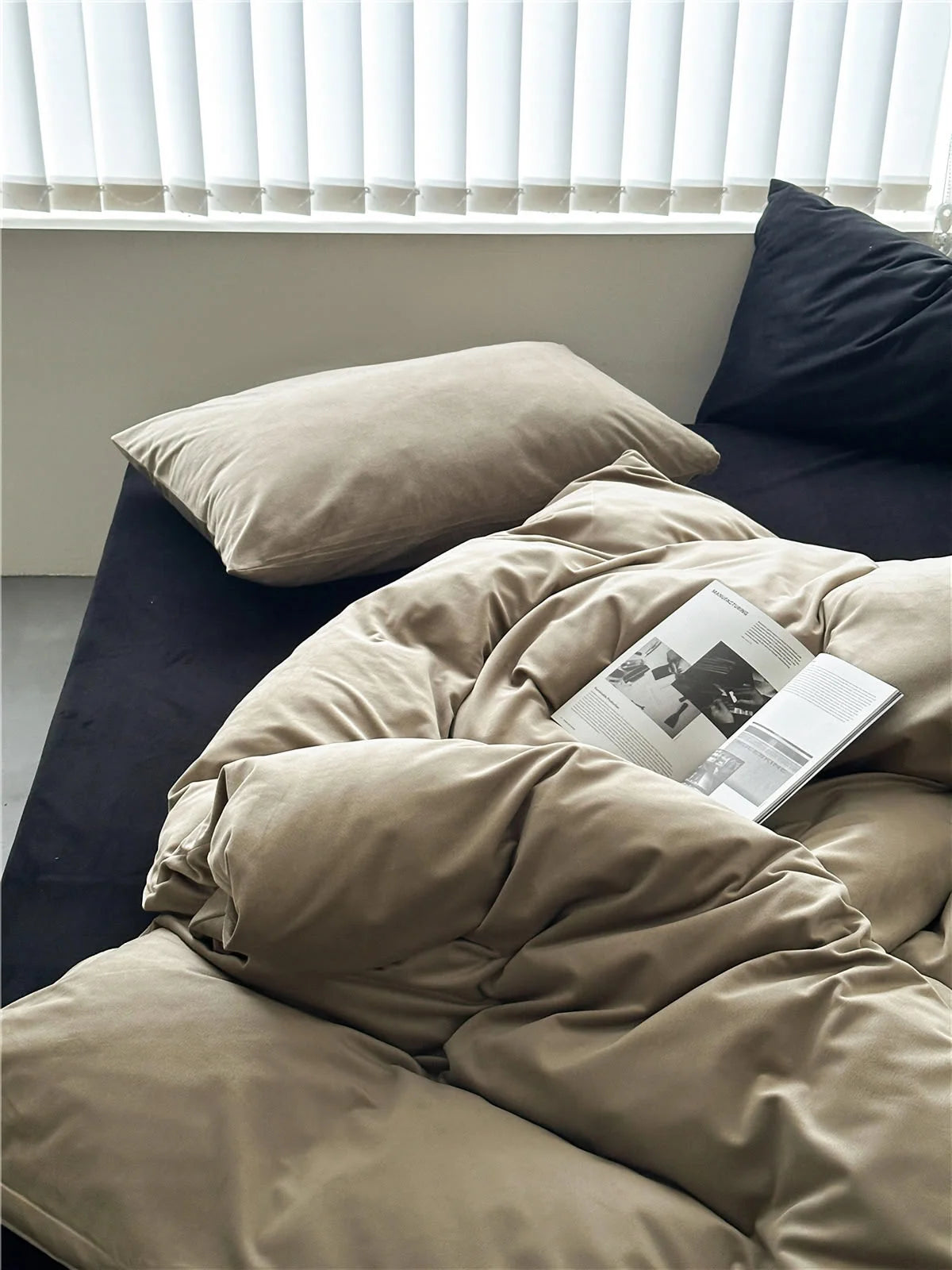 The Warm Beige velvet duvet cover and pillow on a bed with a black sheet, near a window. - RoomDen