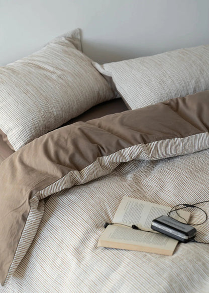 Close-up of the Latte Brown pinstripe bedding with an open book, showcasing its soft texture - RoomDen