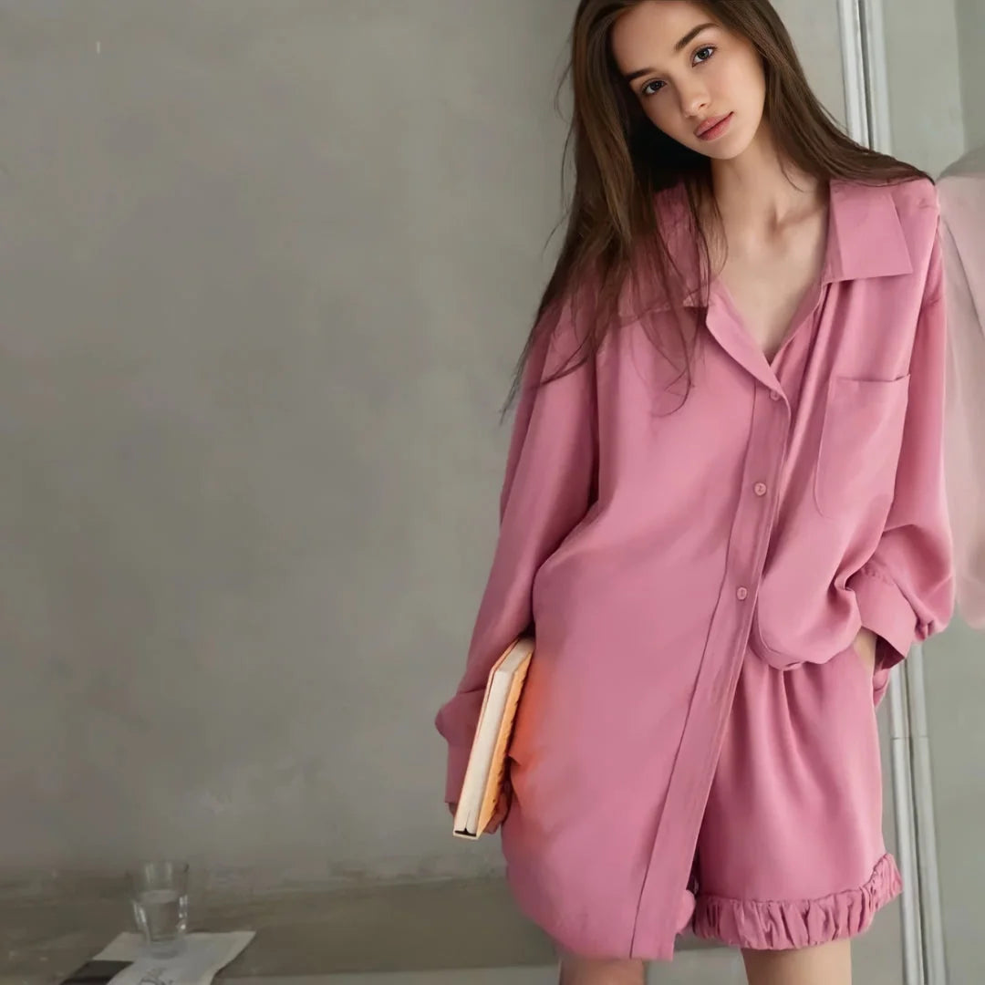 A full-body shot of a model holding a book, wearing the long-sleeve pink pajama set with ruffle shorts. - RoomDen