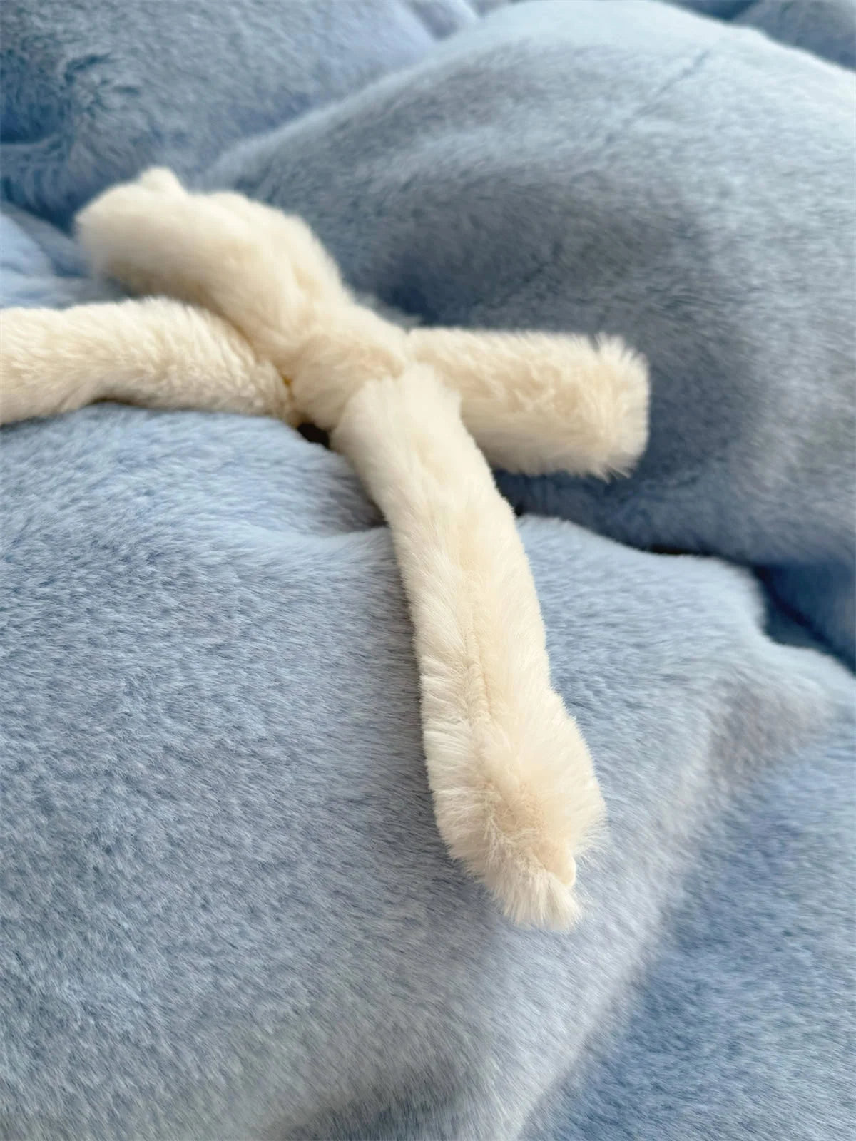 Extreme close-up on a white plush bowknot detail on the blue fleece comforter.