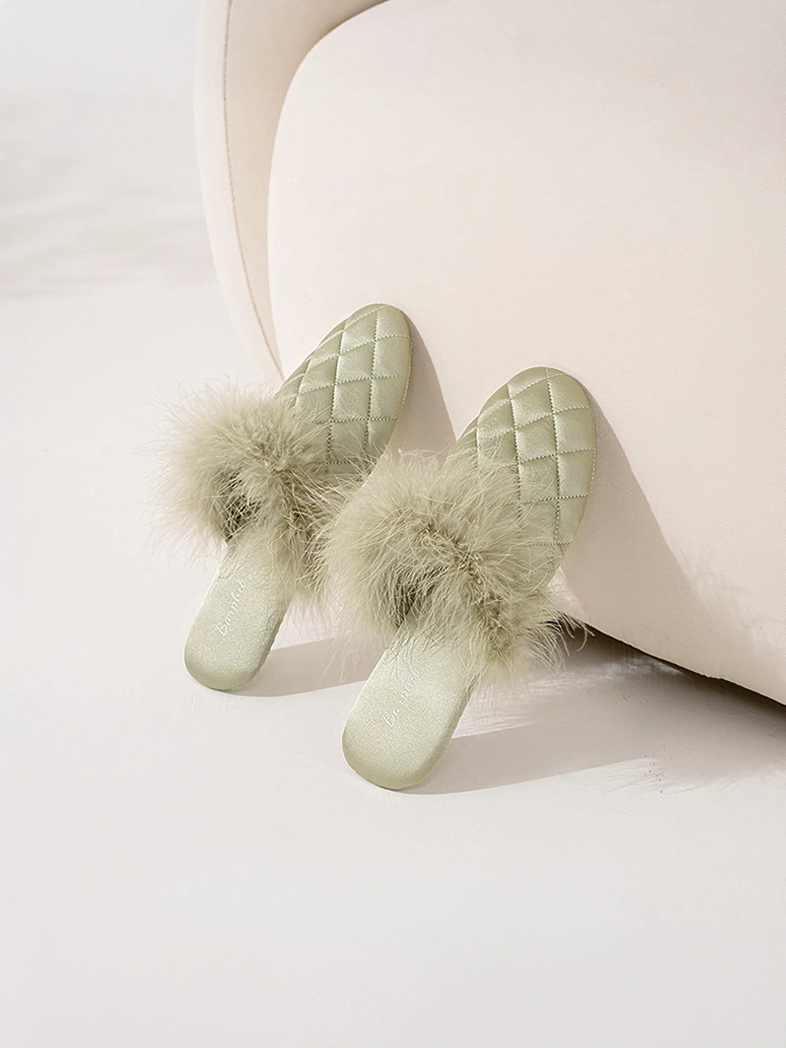 Pair of sage green feathery slippers styled on white background - RoomDen