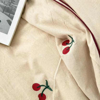 Close-up detail of the red and green embroidered cherry on the textured creamy beige washed cotton fabric.