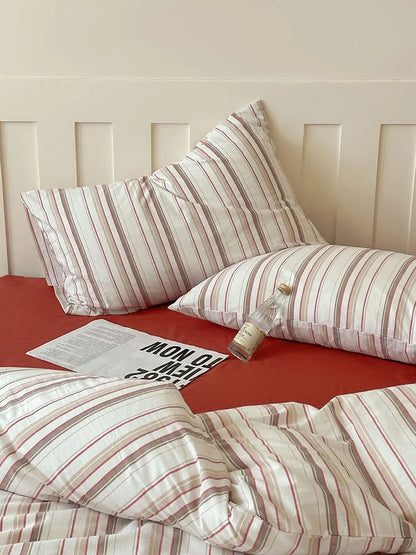 Detail shot of the Red Pinstripe Washed Cotton pillowcases on a bed with a red sheet. - RoomDen