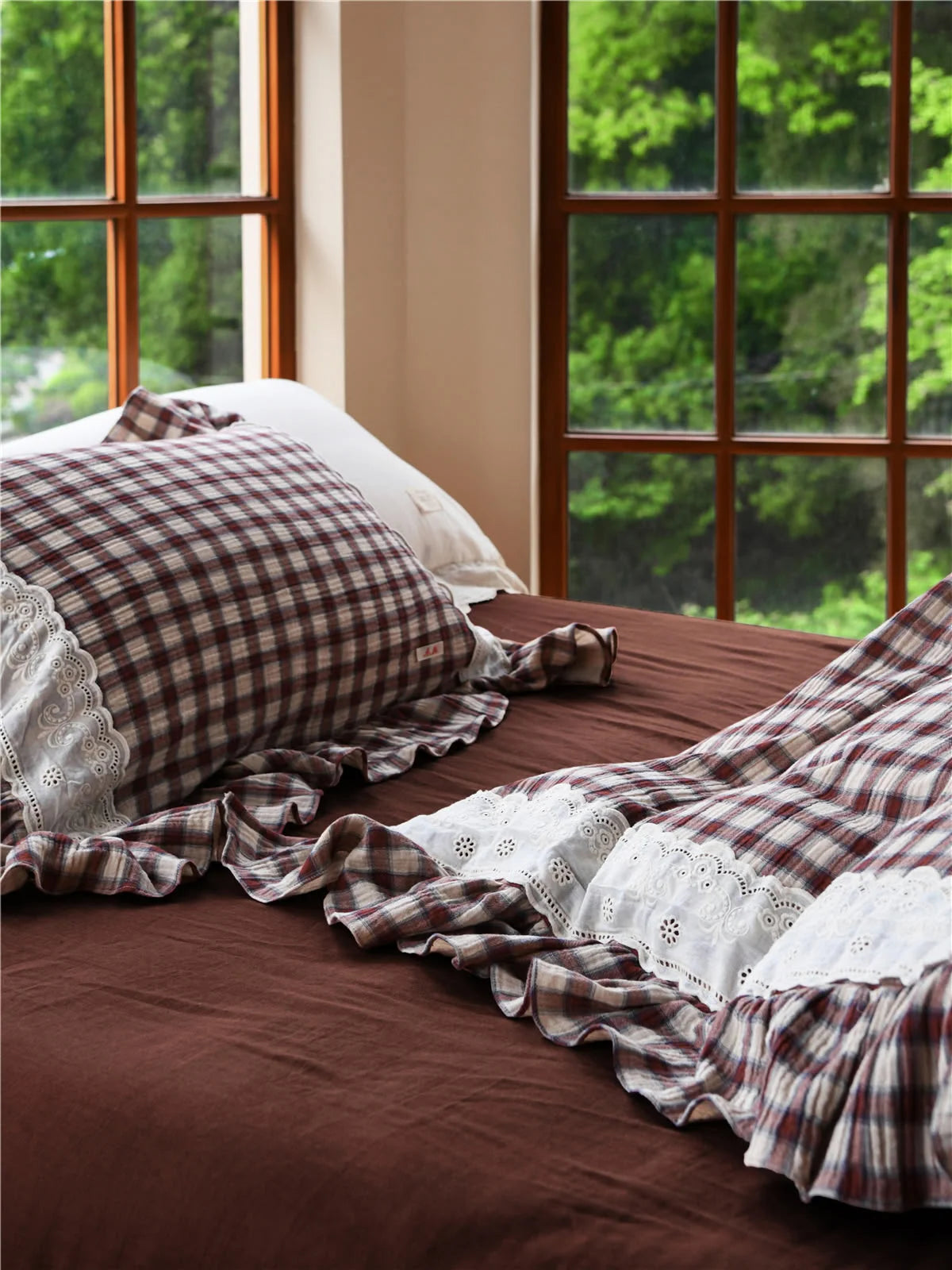 Detail of the Brown Gingham duvet cover and pillow sham against a dark brown sheet by a window.
