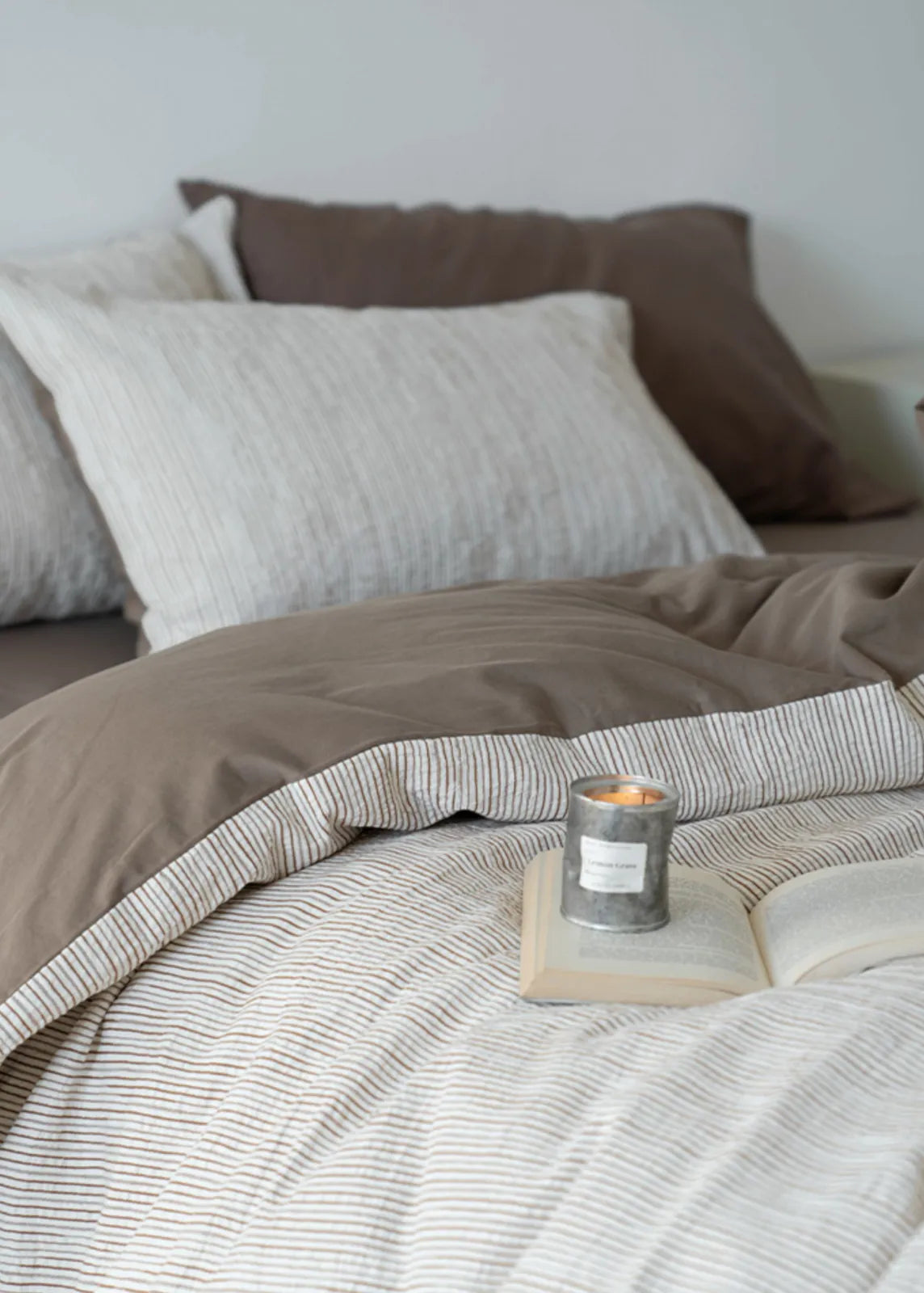 Lifestyle image of the Latte Brown pinstripe bedding with a lit candle on a book, creating a Hygge mood.