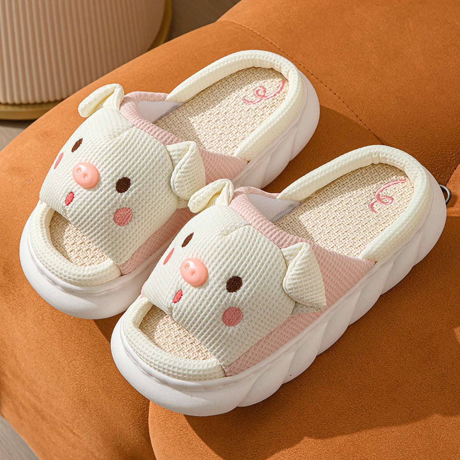 Close-up of White Waffle Textured Embroidered Pig Linen House Slippers showing pink snout details on an orange sofa - RoomDen