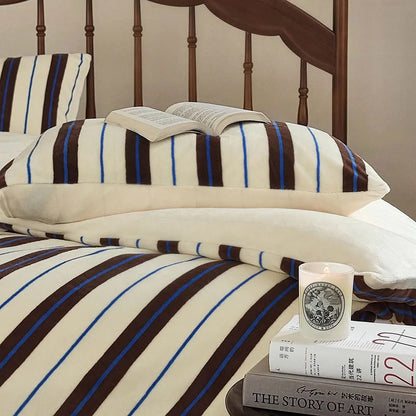 A book resting on the cream and brown striped velvet pillow, highlighting its cozy vibe - RoomDen.
