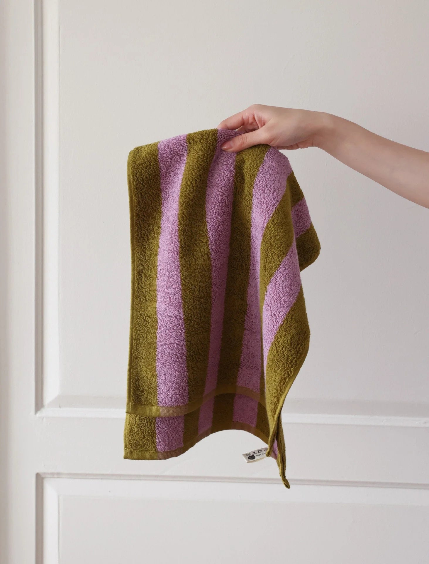 Plush Bold Striped Cotton Towel in green and purple held up against a white wall. - RoomDen