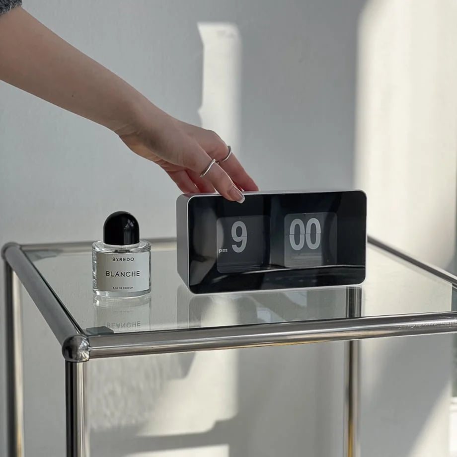 A hand adjusting the black and white automatic flip clock on a modern glass table. - RoomDen