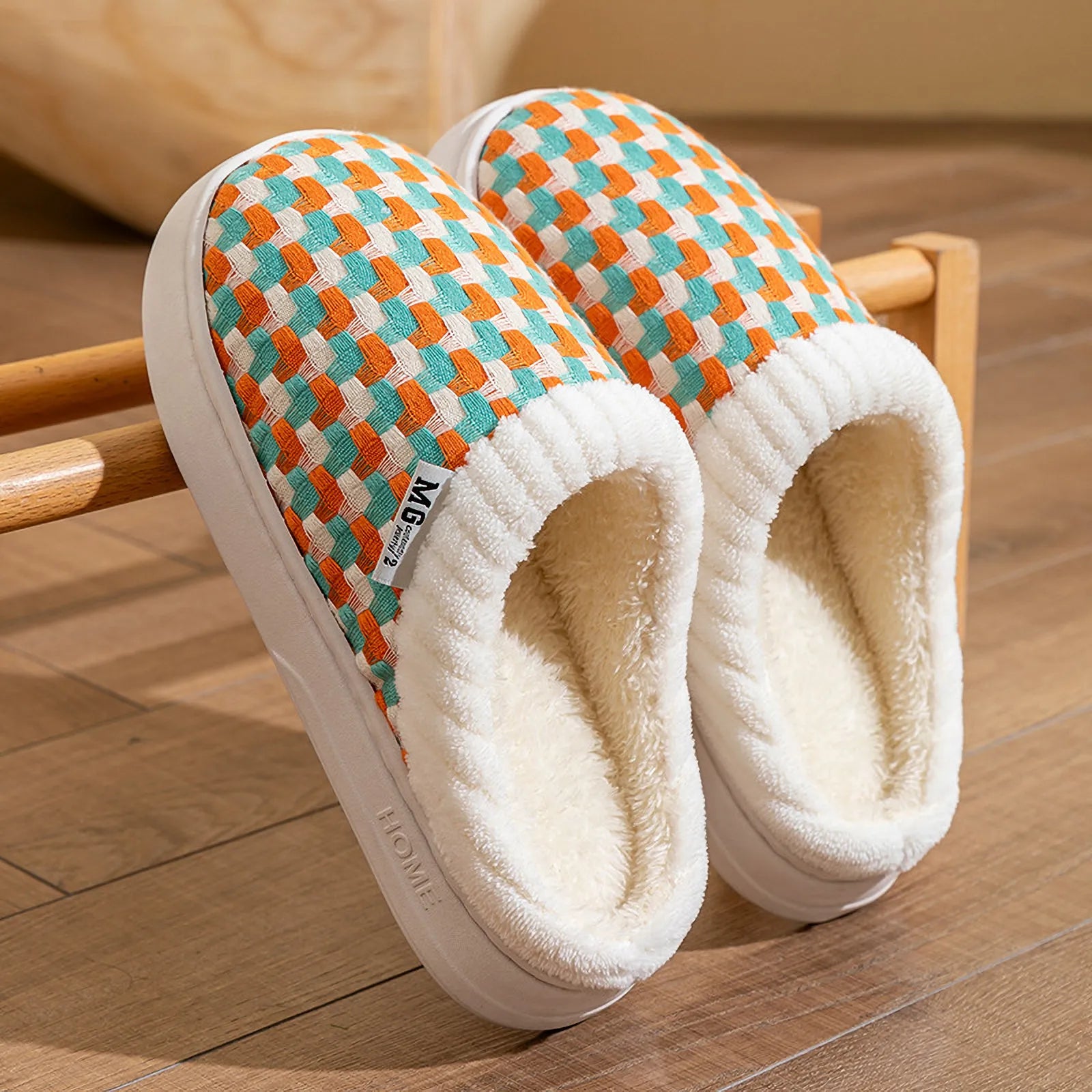 Pair of multi-color orange and teal woven plush slippers on wooden rack