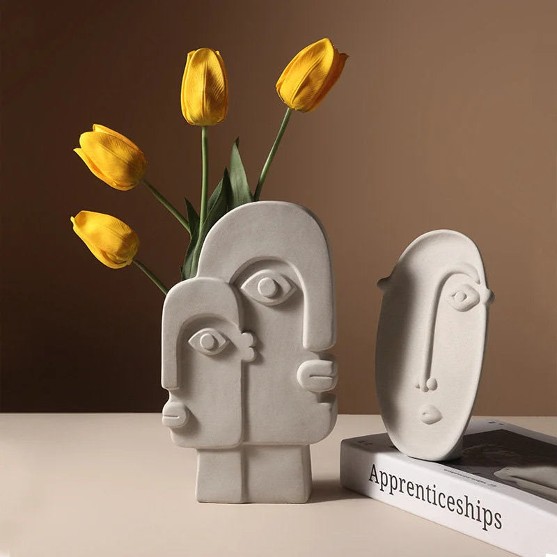 Two Japandi-style abstract face vases, one holding yellow tulips, next to a book - RoomDen.