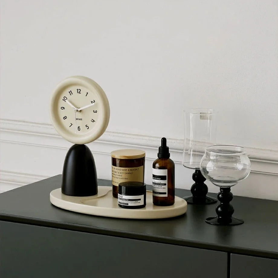 Sculptural black and beige wood table clock on a dark console table with decor items. - RoomDen