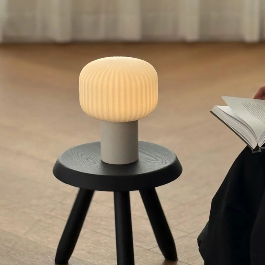Pleated Glass Mushroom Accent Lamp glowing warmly on a black stool in a cozy room - RoomDen
