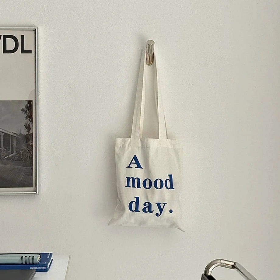 Front view of the sleek silver cylindrical wall hook holding a white tote bag against a clean white wall. - RoomDen