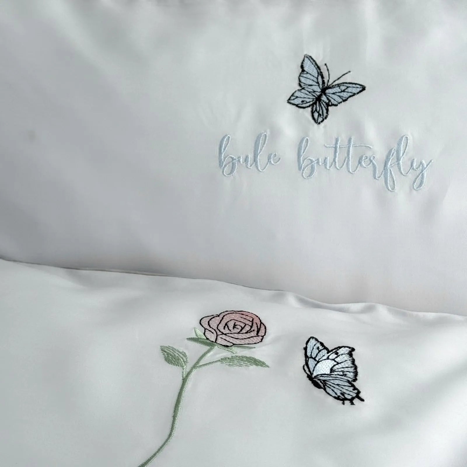 Detailed shot of the pillowcase and duvet cover, showing the "blue butterfly" text embroidery and the rose and butterfly motifs.
