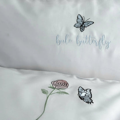 Detailed shot of the pillowcase and duvet cover, showing the "blue butterfly" text embroidery and the rose and butterfly motifs.