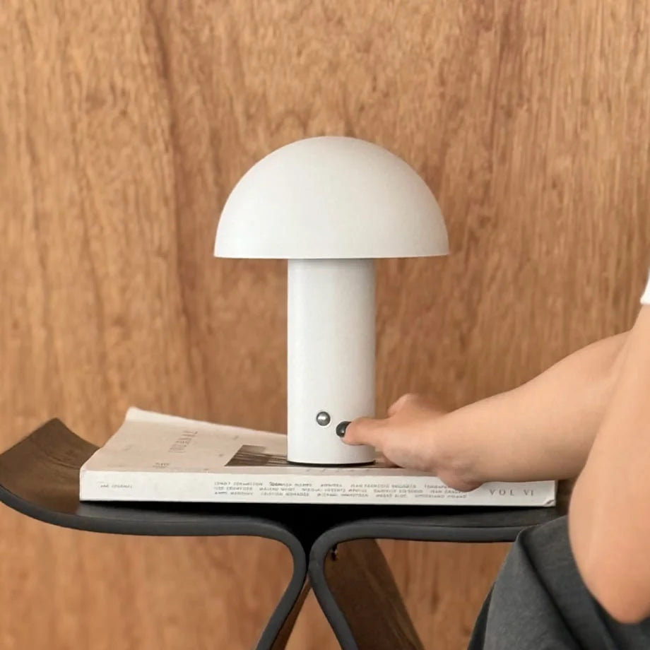 A finger pressing the control button on the white metal mushroom lamp to change the light setting - RoomDen.