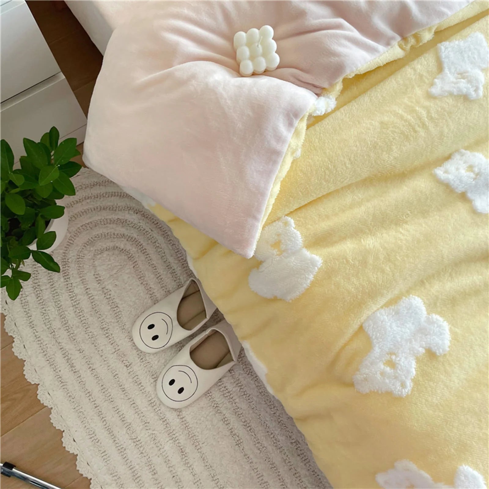 Overhead view showing the corner of the yellow teddy bear bedding, a pink pillow, and cute smiley-face slippers on a rug. - RoomDen