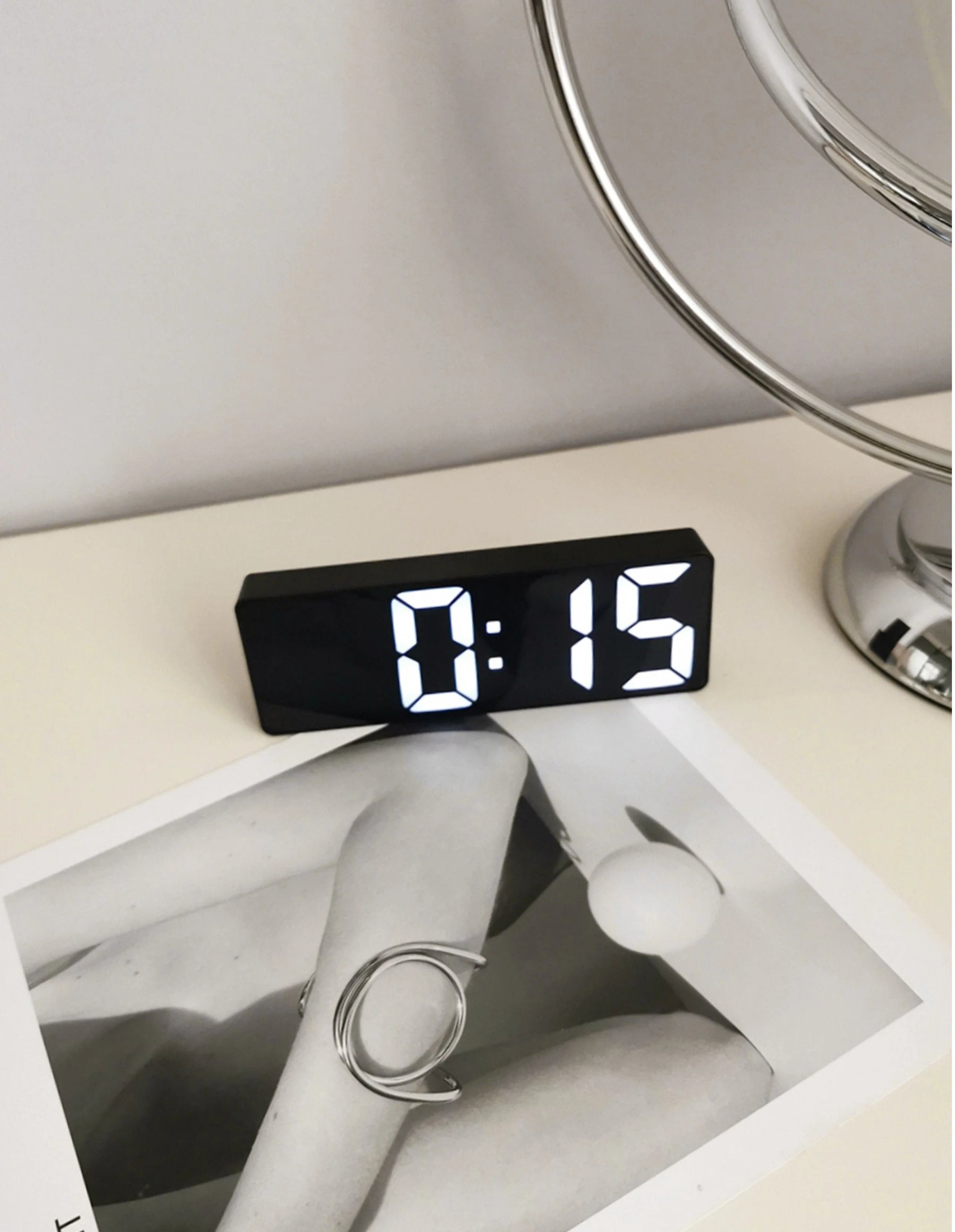 The black Sleek Mirrored LED Table Clock on a white desk next to a chrome lamp and modern decor. - RoomDen