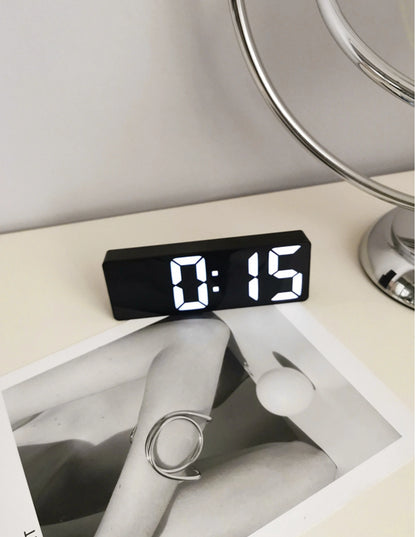 The black Sleek Mirrored LED Table Clock on a white desk next to a chrome lamp and modern decor. - RoomDen