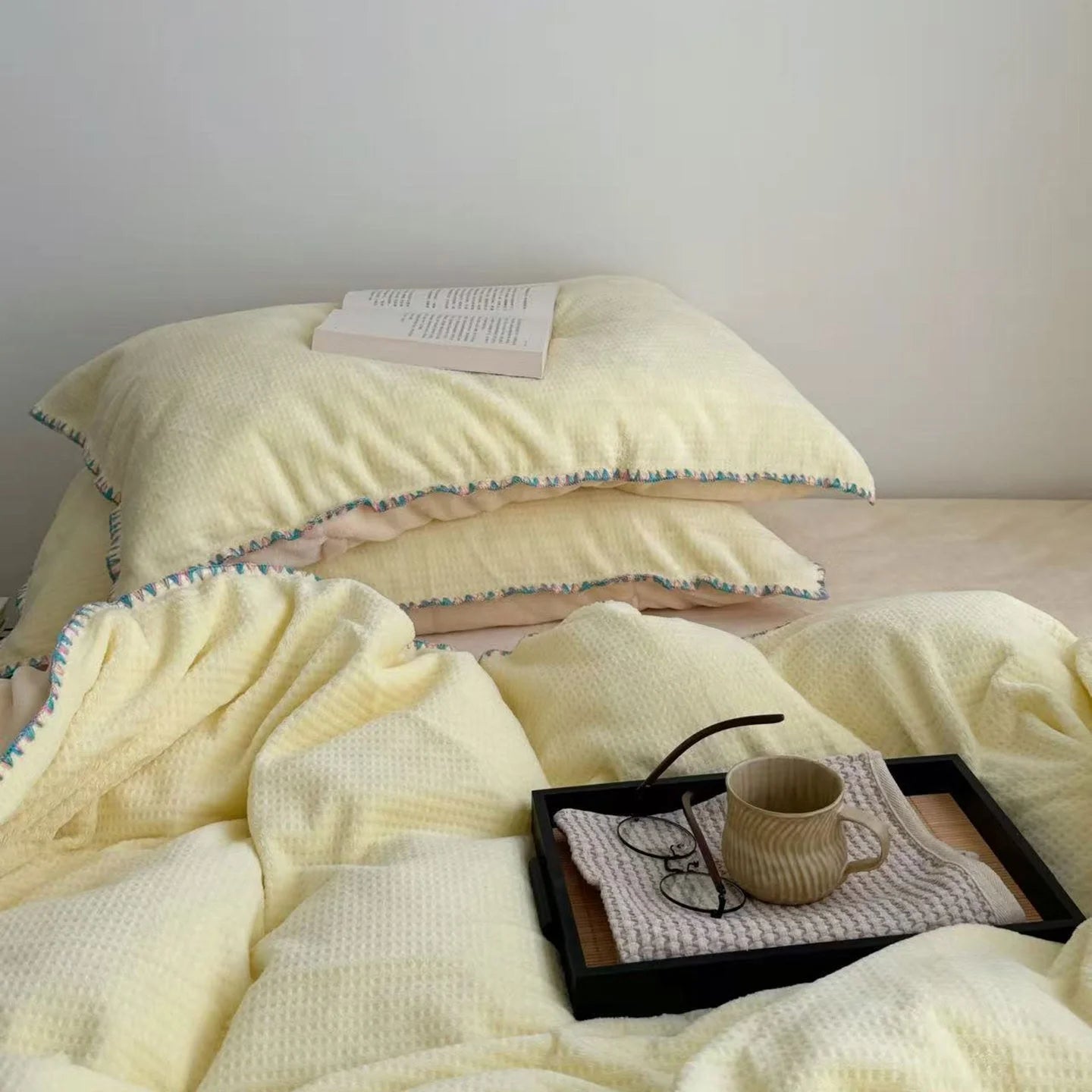 Top-down view of the Butter Yellow Waffle Fleece pillowcases and duvet cover with a tray and glasses.