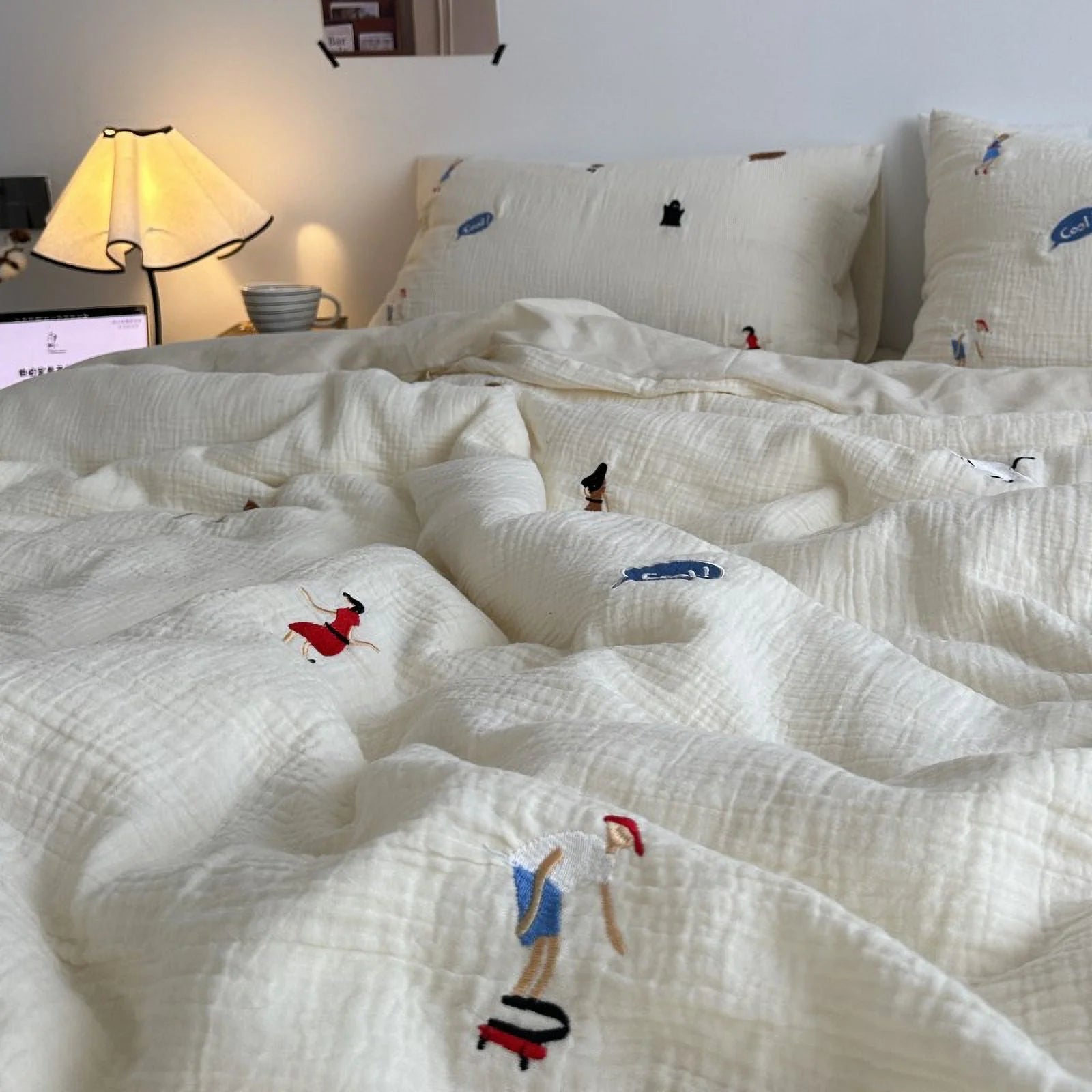 The whimsical embroidered cream bedding set in a cozy bedroom setting with a warm lamp lit. - RoomDen