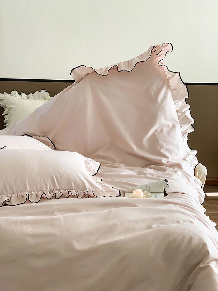 Detail shot of the corner of the Blush Pink ruffled pillow, highlighting the delicate black trim and fabric texture - RoomDen.