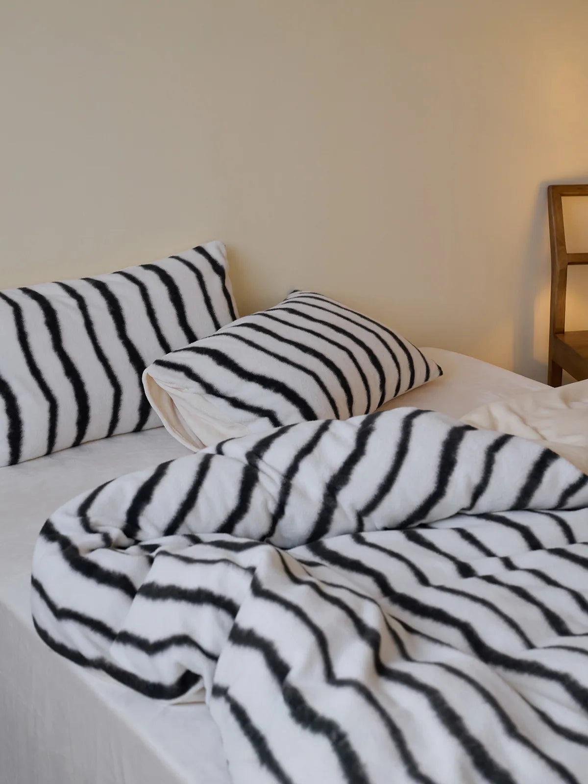 Side view of a bed with a plush black and white striped flannel fleece duvet and pillowcases, showing the texture - RoomDen.