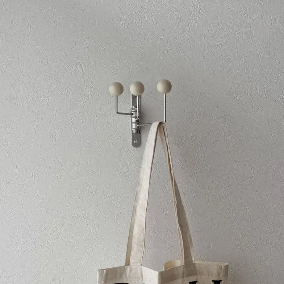 The cream metal ball-end hook mounted on a white wall, shown with a canvas tote bag - RoomDen.