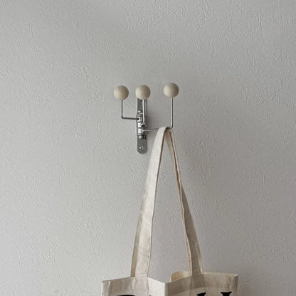 The cream metal ball-end hook mounted on a white wall, shown with a canvas tote bag - RoomDen.