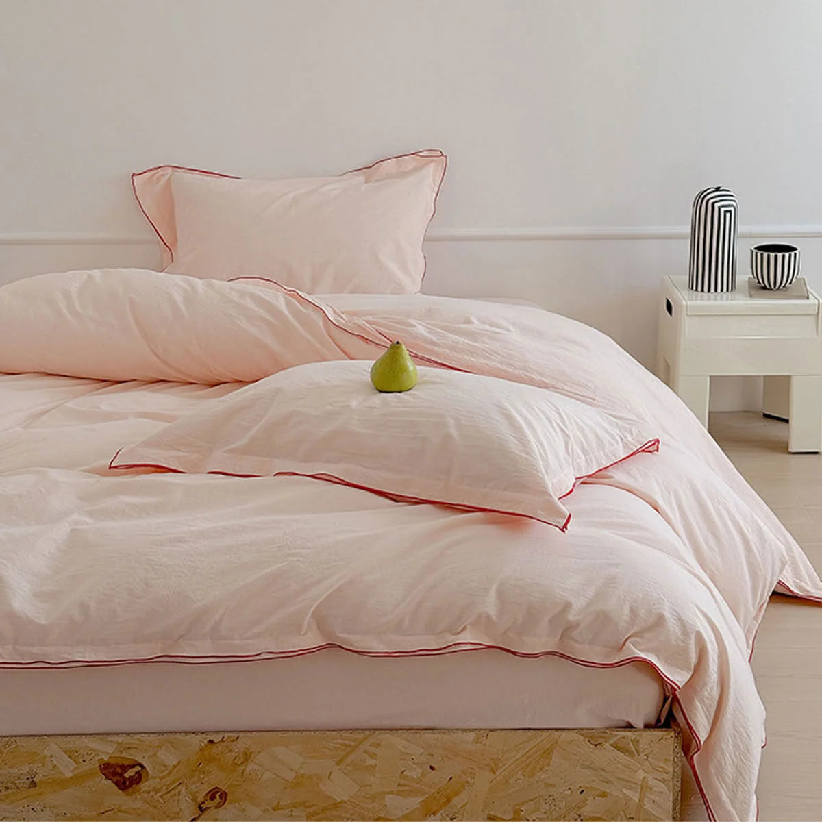 Lifestyle shot of the blush pink washed cotton bedding set, showing a bedside table with a striped vase.
