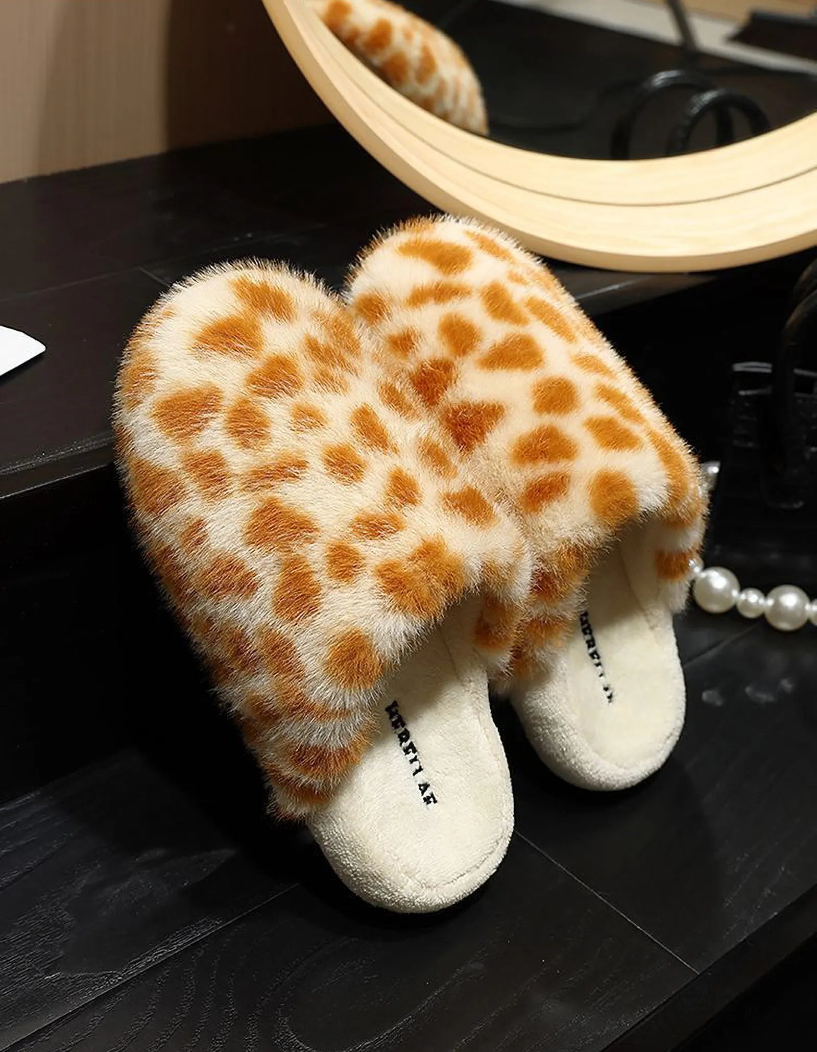 Pair of Beige & Brown Spots giraffe print fuzzy slippers on black shelf