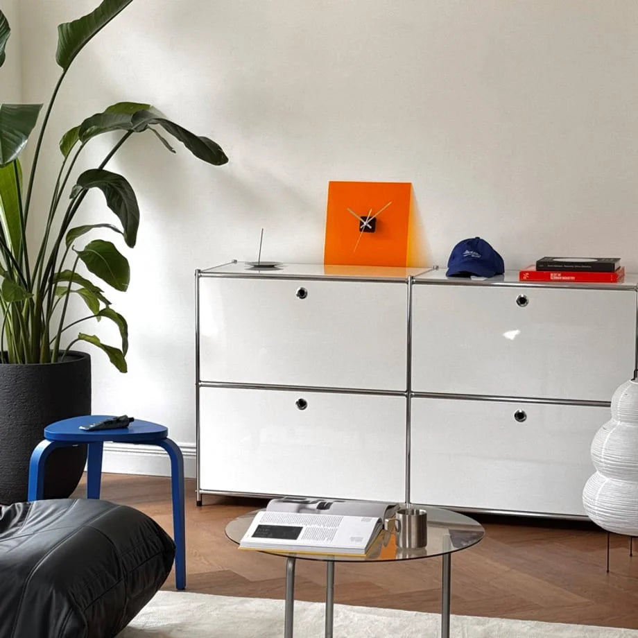 Vivid Orange acrylic clock on a modern cabinet with a large plant and beanbag chair nearby. - RoomDen