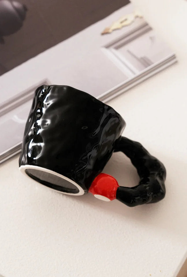 Close-up detail of the glossy black ceramic mug with red accent bead, showing the irregular texture - RoomDen.