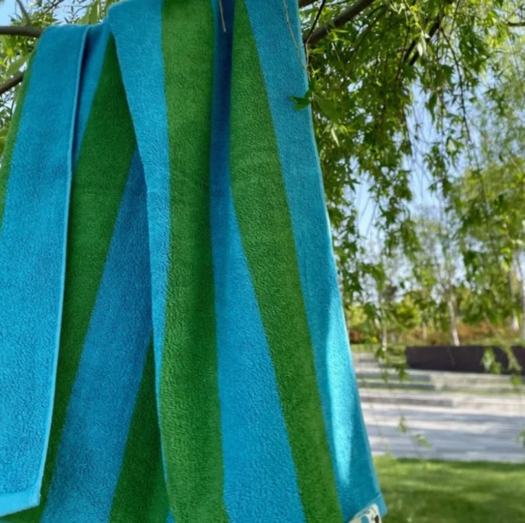 A vibrant blue and green striped cotton towel hanging from a tree branch outdoors on a sunny day. - RoomDen
