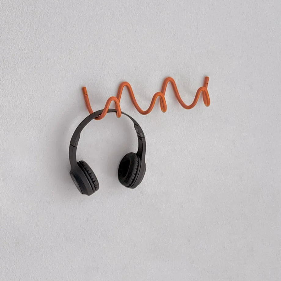 Close-up of black headphones hanging on the bright orange Wavy Coil Metal Wall Hook. - RoomDen