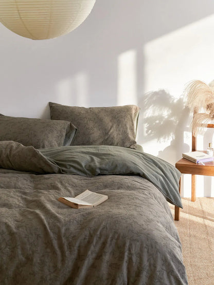 A serene bedroom scene featuring the Textured Botanical Washed Cotton Bedding Set, with a paper lantern overhead and a book resting on the duvet - RoomDen.