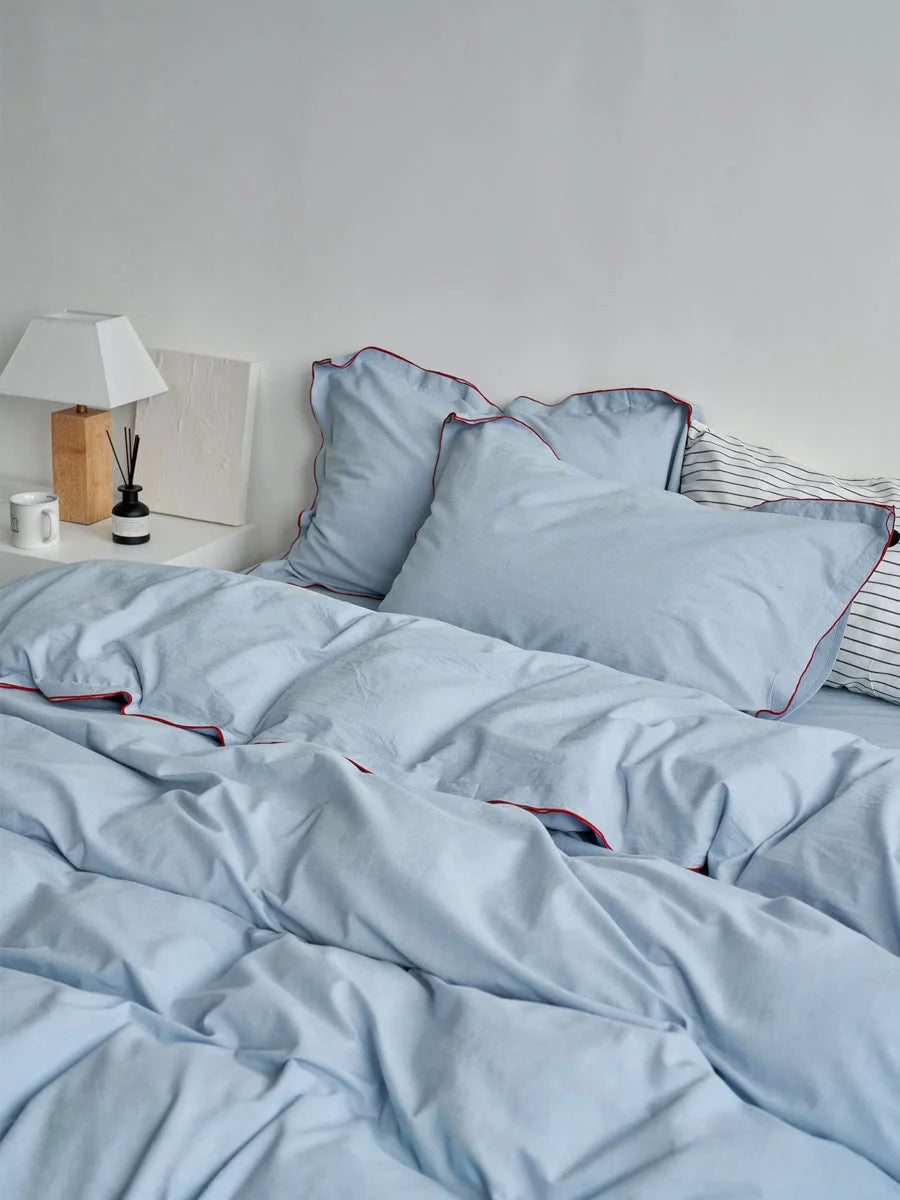 Full view of a bed with a sky blue washed cotton duvet cover, showing the bedside table with a lamp and diffuser.
