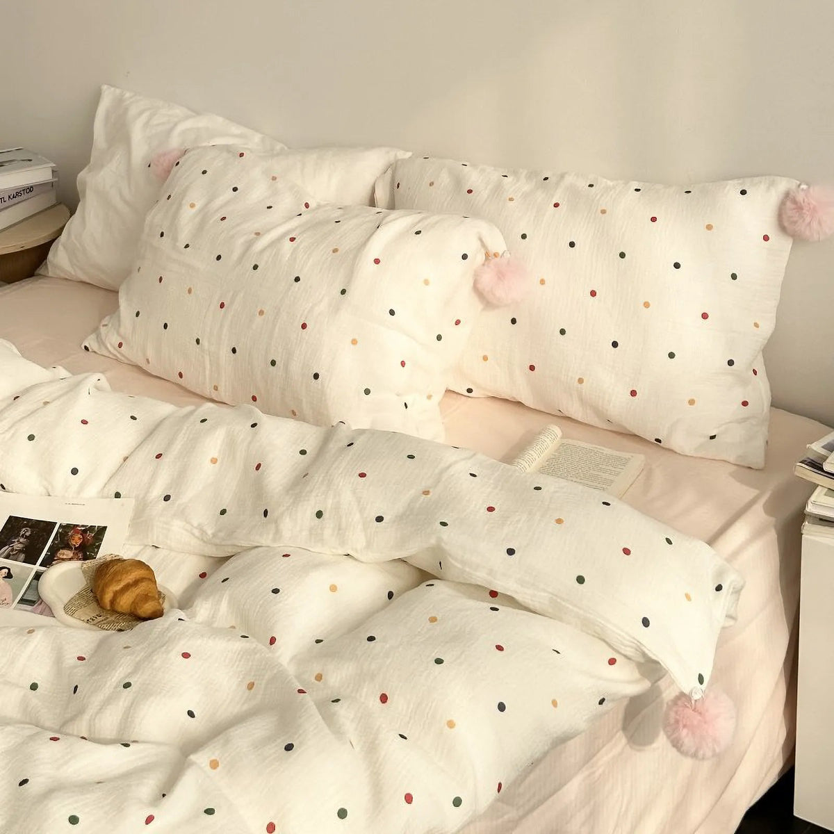 A full view of the white and colorful polka dot bedding set on a bed, showing the duvet cover and two pillows with pink pom-poms. - RoomDen
