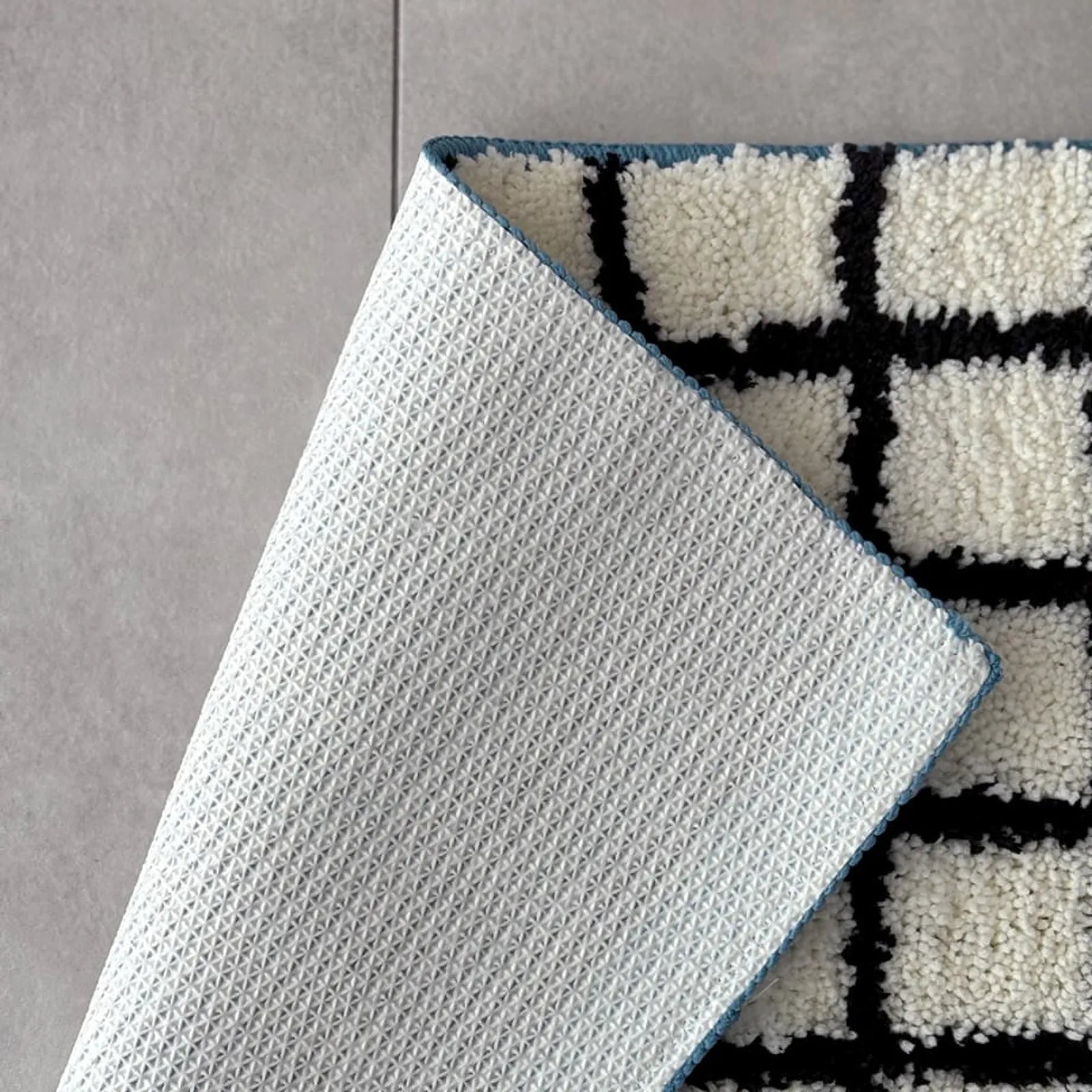 Close-up detail of the rug's white non-slip backing showing textured grip dots - RoomDen